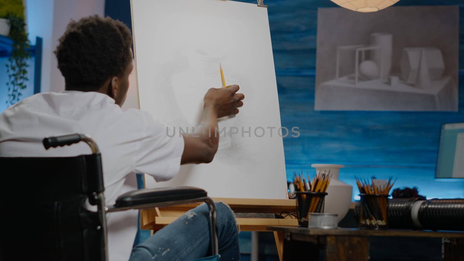 African american disabled young artist drawing vase on canvas and easel while sitting in wheelchair at workshop studio. Black paralyzed person with disability working on fine art concept