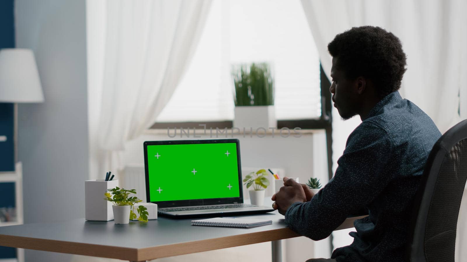 African american man using mockup laptop with green screen. Computer user on isolated chroma key mock up display in living room, bright house. E commerce and online shopping