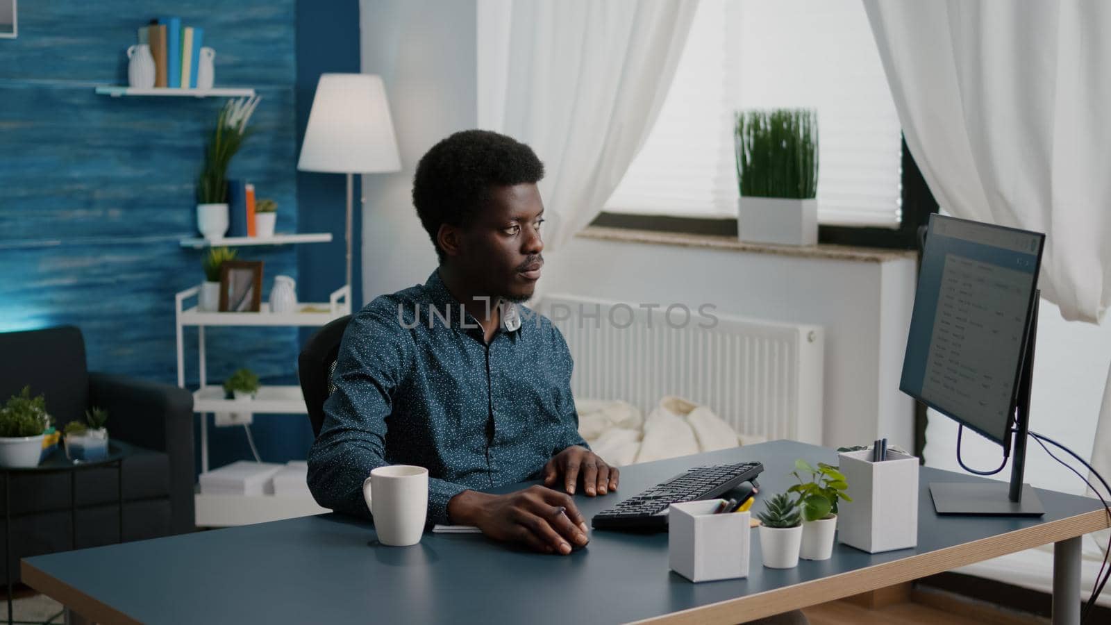 Black african american freelancer taking notes on notepad and looking into computer, remote working from home computer user