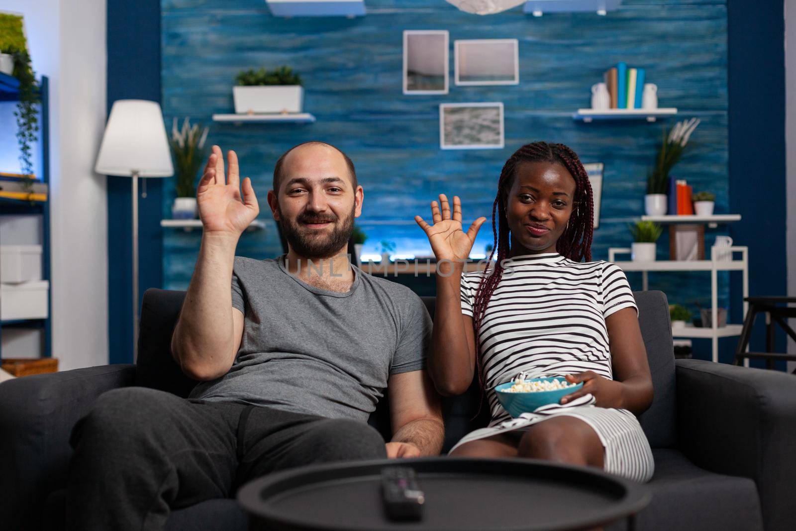 Interracial couple waving at video call camera using technology for online remote communication on internet. Multi ethnic partners talking to friends on video conference at home