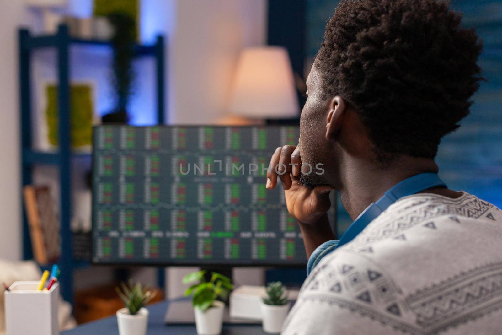 African american trader worker checking stock market chart on computer developing investment strategy. Young man broker trading crypto currency working remote from home. Investment data on screen