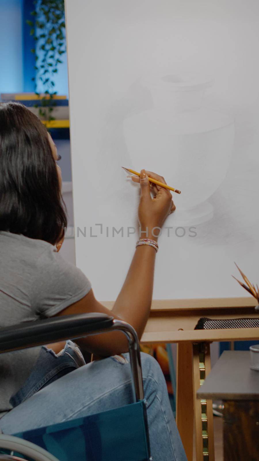 Black invalid artist with handicap using pencil on canvas for authentic vase drawing at studio. African american disabled woman sitting in wheelchair while working on new masterpiece
