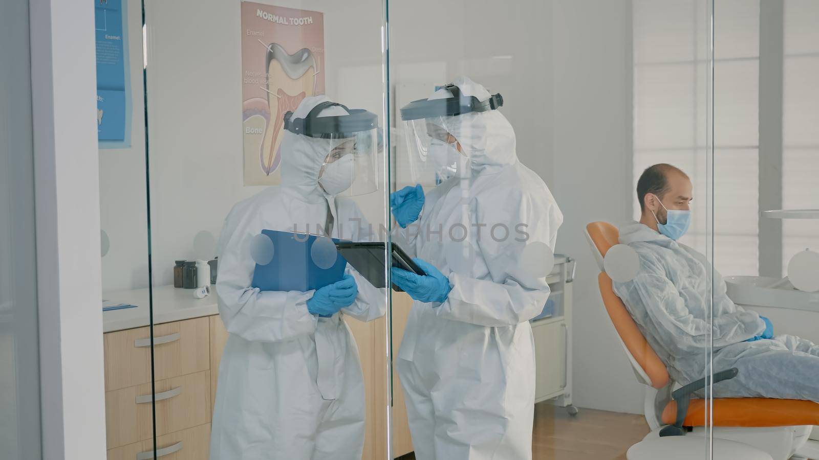 Team of dentists with ppe suits holding tablet for teeth consultation at dental clinic. Orthodontists wearing coverall, face shield and gloves using digital technology for oral care