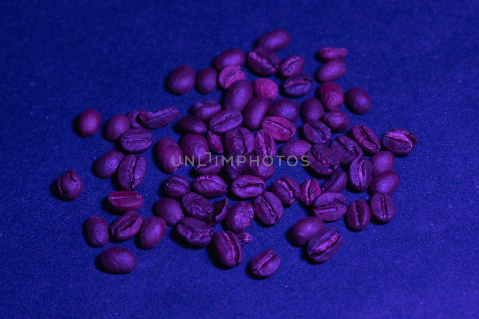 roasted coffee beans are casually scattered on a dark blue background under a blue light on a flat surface