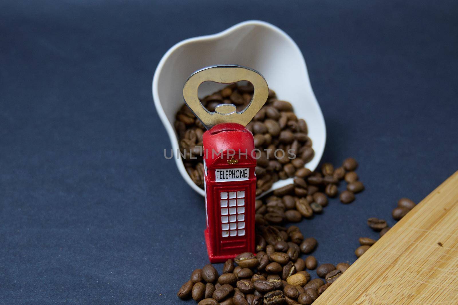 roasted coffee beans on a black background next to a bottle opener in the form of an English telephone booth in red