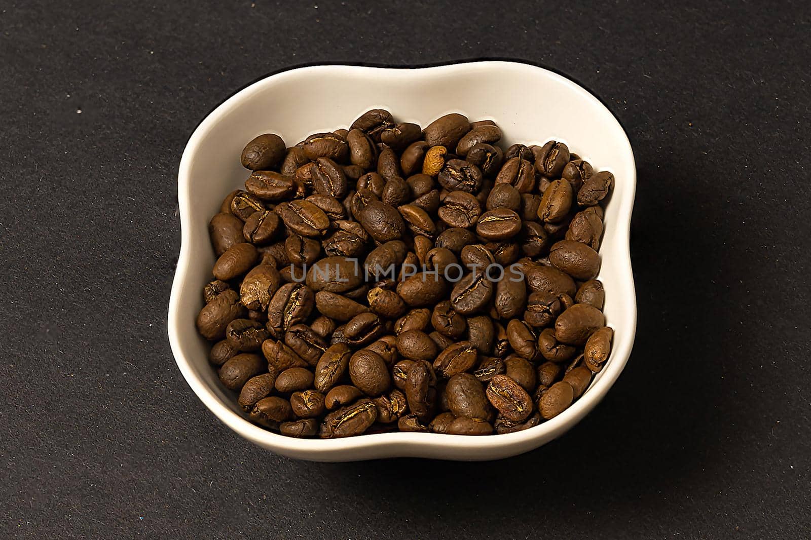 roasted coffee beans are poured into a white porcelain bowl and placed on a black background