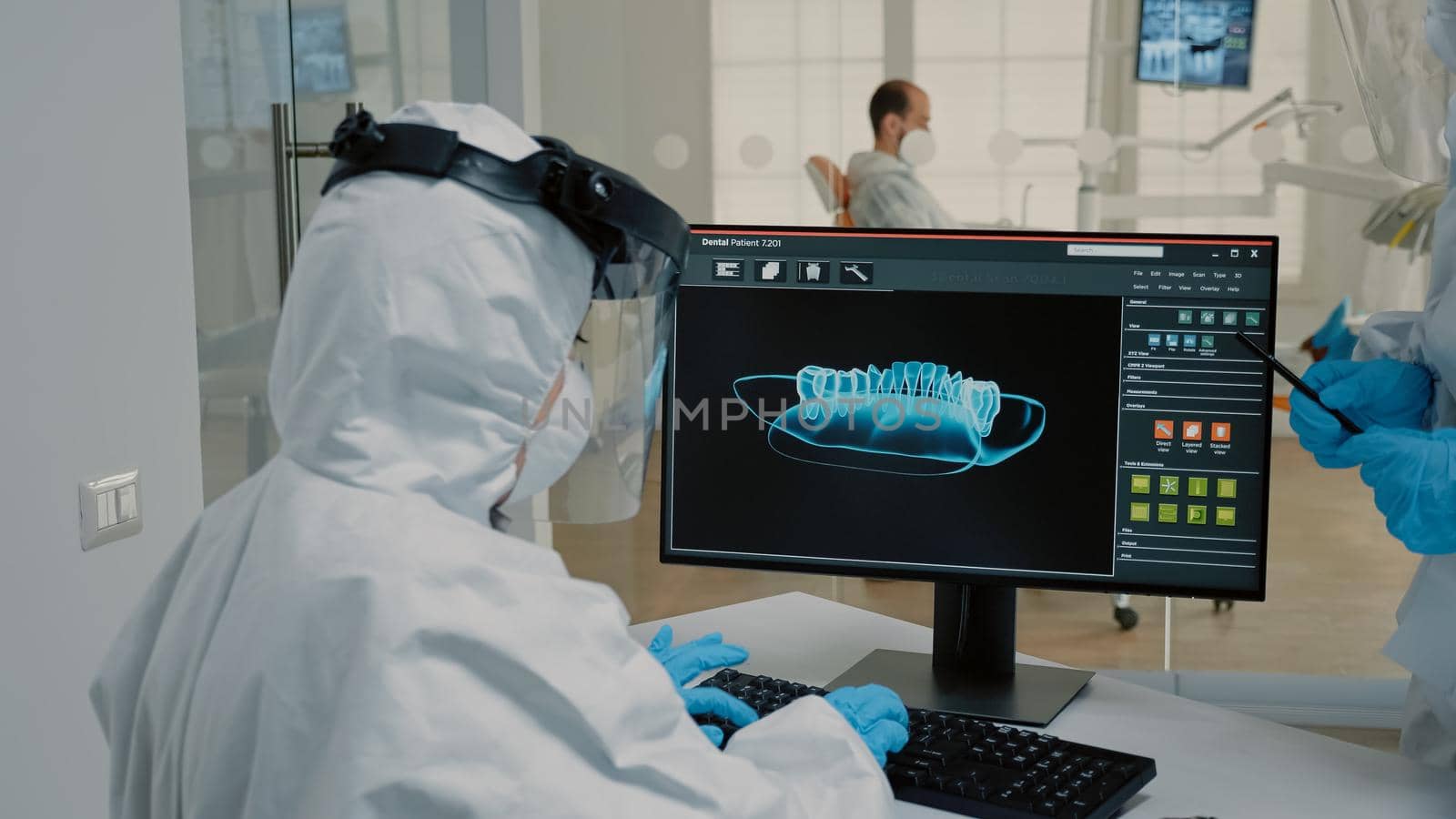 Team of orthodontists examining radiography of dentition on modern computer monitor at oral clinic. Stomatologist and assistant using dental x ray scan for teeth hygiene on patient