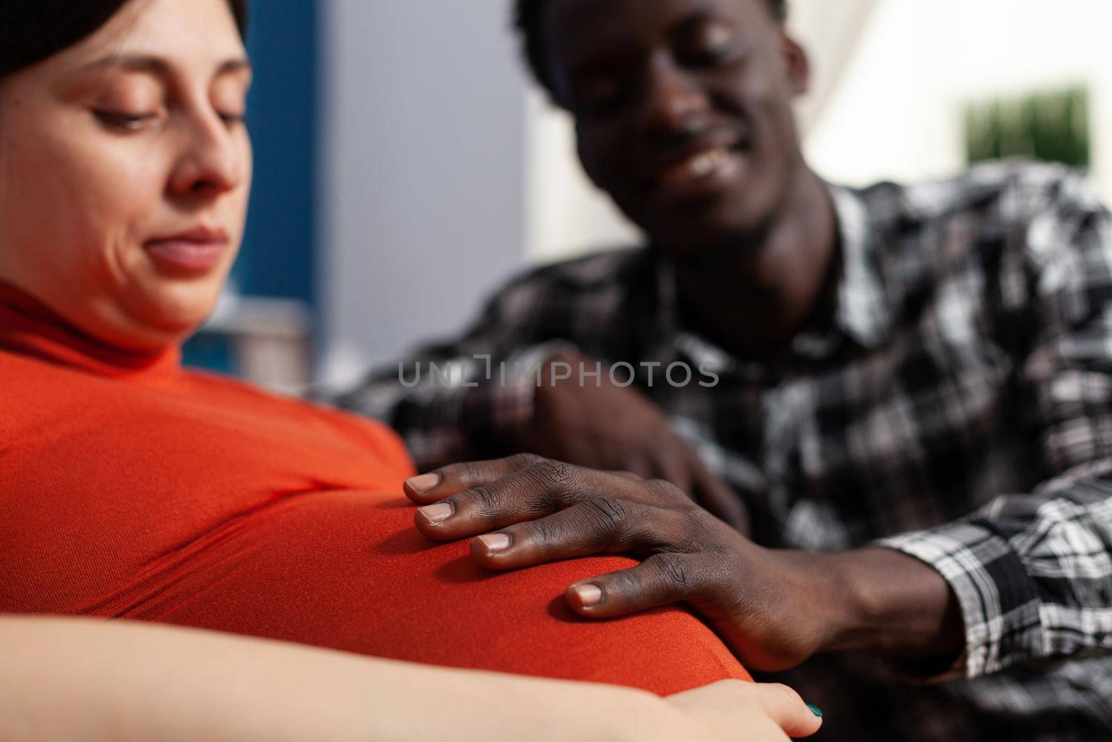 Close up of black father of child touching belly of pregnant woman. African american man holding hand on baby bump smiling about parenthood. Interracial couple with pregnancy.