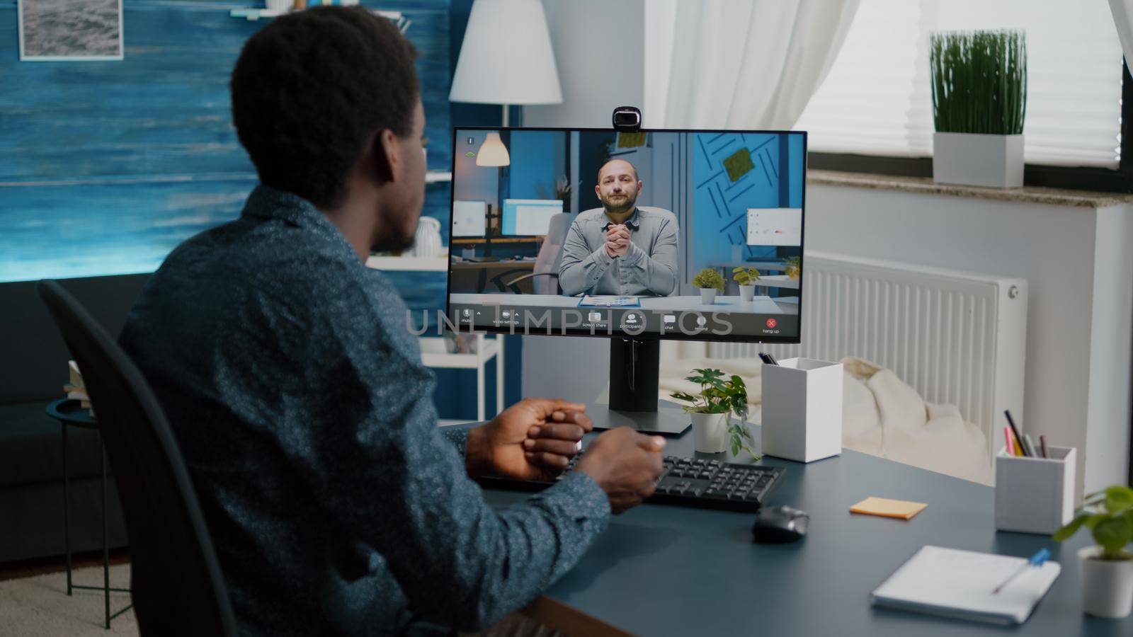 African american man chatting using online web internet communication while working from home office. Remote worker on online video conference with his boss talking via webcam