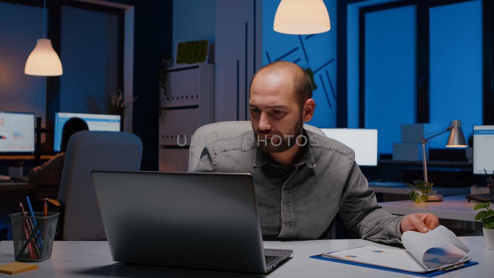 Exhausted workaholic businessman analysing marketing statistics in startup office late at night. Overworked entrepreneur working on financial strategy before company deadline, corporate business management