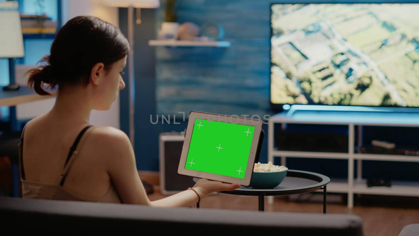 Young person looking at tablet with horizontal green screen background sitting in living room on couch. Woman using chroma key with isolated copy space for mockup template and copy space