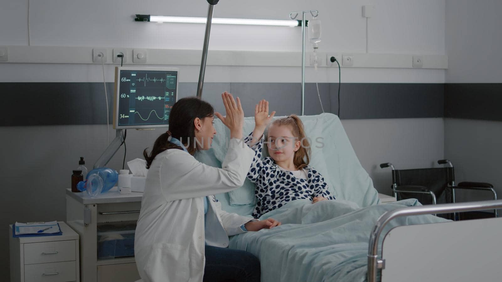 Pediatrician woman doctor relaxing while playing high five with sick girl patient by DCStudio