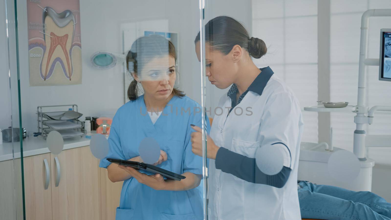 Dentist and assistant analyzing modern tablet screen in dental cabinet. Stomatological staff using technology for patient teethcare and examination. Dentistry team wearing medical uniform