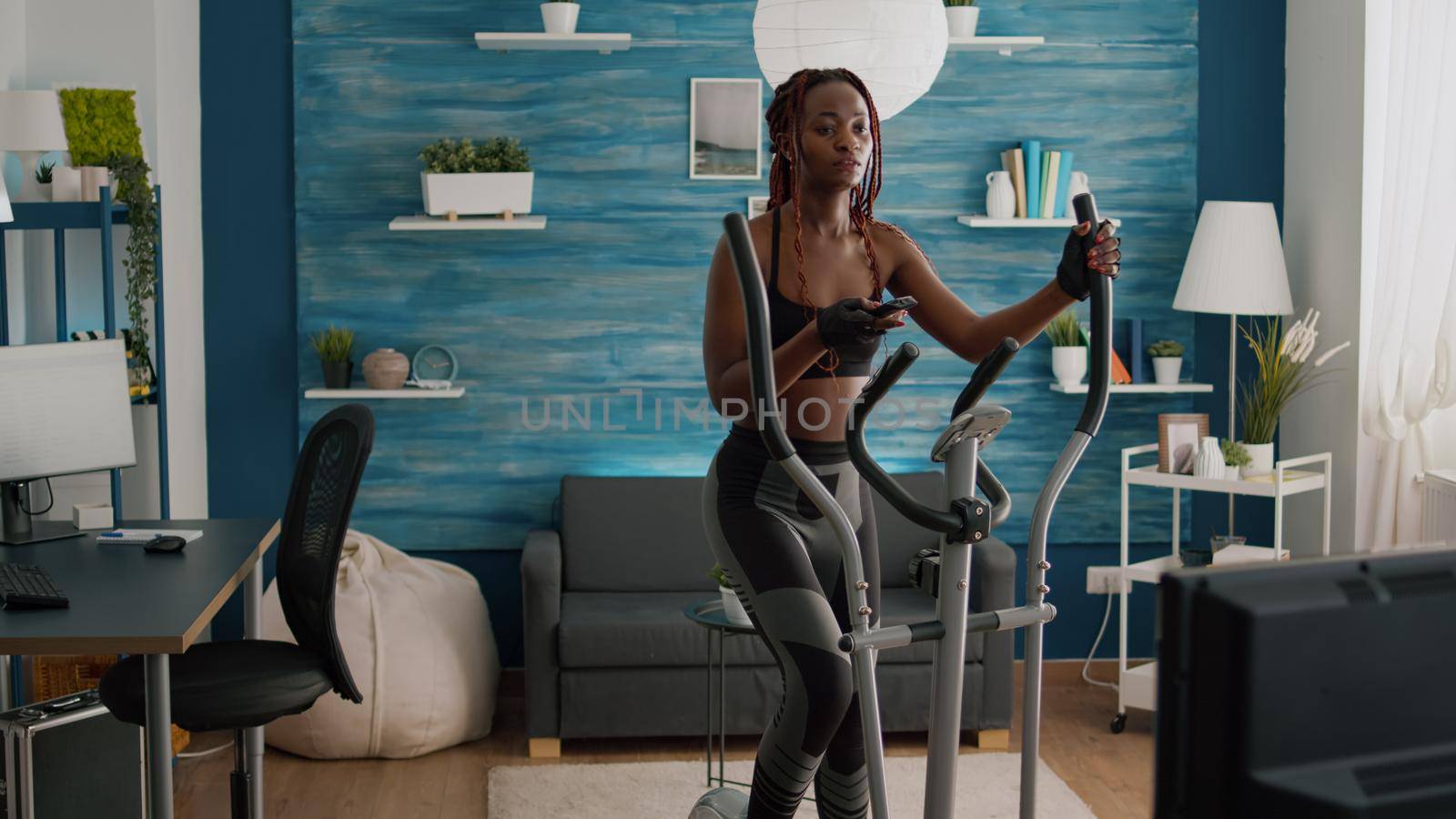 Cyclist woman with black skin in sportswear training body muscle using elliptical by DCStudio