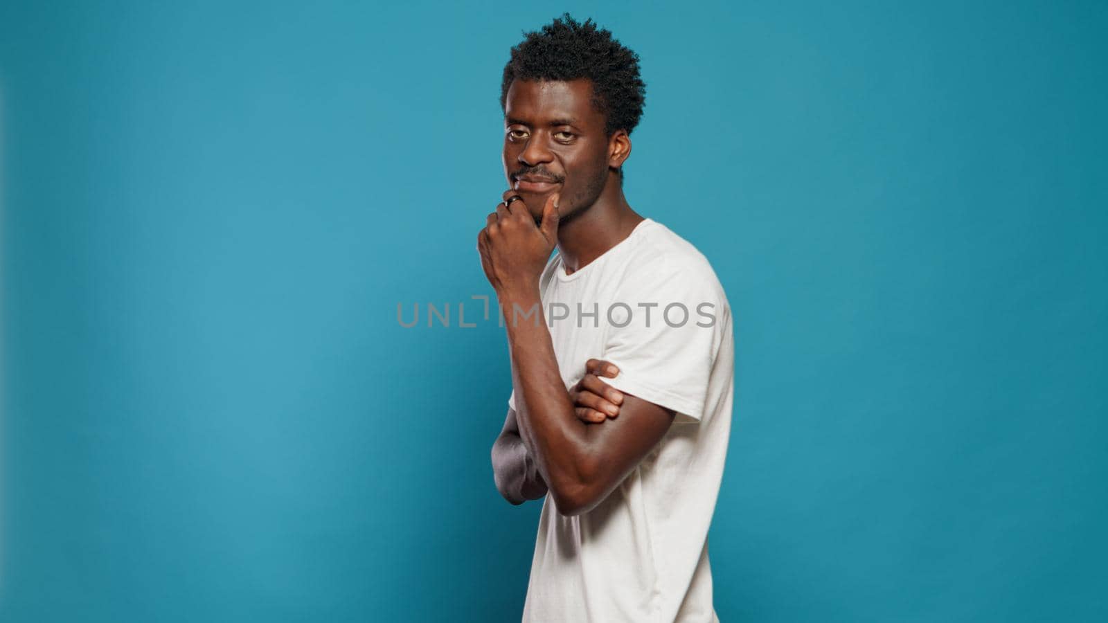 African american man looking at camera and rubbing chin in studio. Black person feeling calm while walking around and having thoughtful expression. Afro posibitive adult with smirk on face