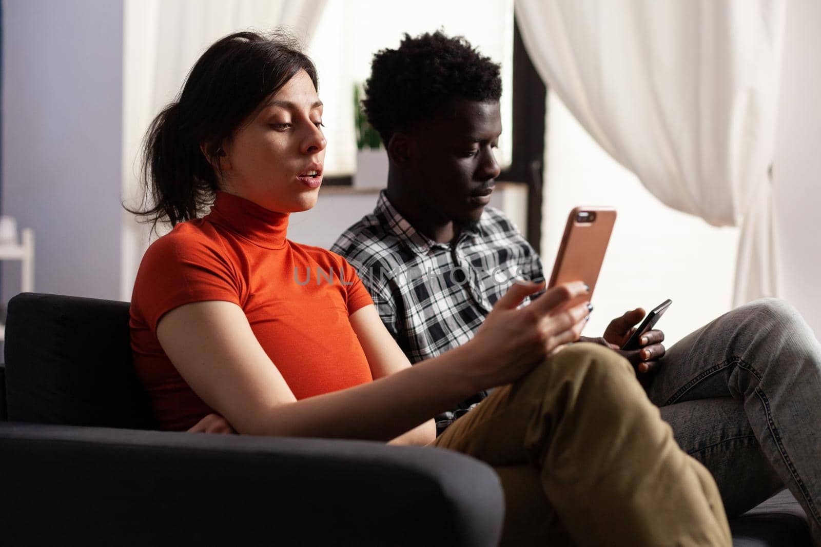 Close up of modern interracial couple using smartphones at home. Multi ethnic lovers holding digital devices with technology. Multiracial people having gadgets with online internet.