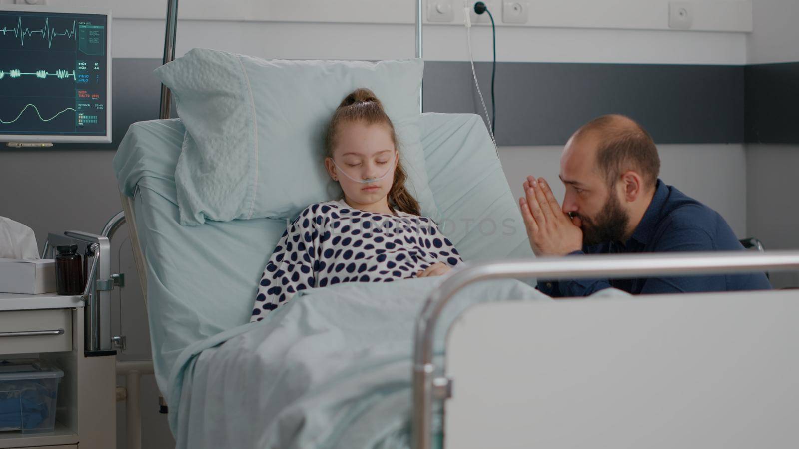 In hospital ward little child patient sleeping while worried father praying for disease recovery waiting for healthcare treatment. Children wearing oxygen nasal tube during medical examination