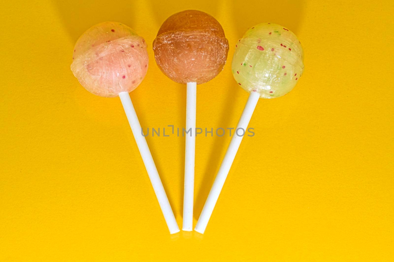 Set of lollipops on yellow background. Big bright tasty lollipops on white sticks on yellow background with copy space. Sweet candy concept.