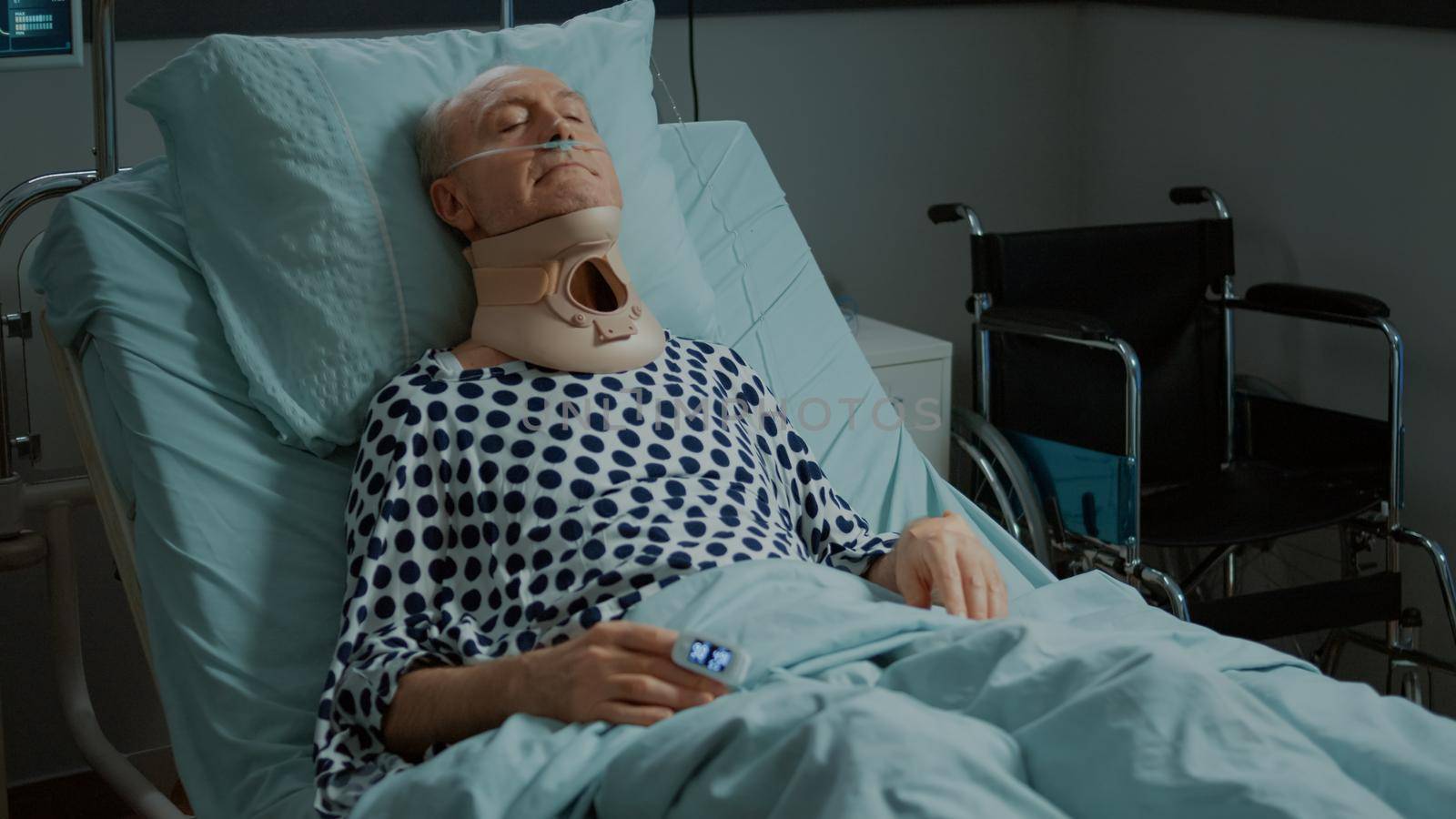 Elder patient sitting in hospital ward bed with cervical collar on neck for injury recovery at emergency room. Sick old man with nasal oxygen tube and oximeter healing from health problems