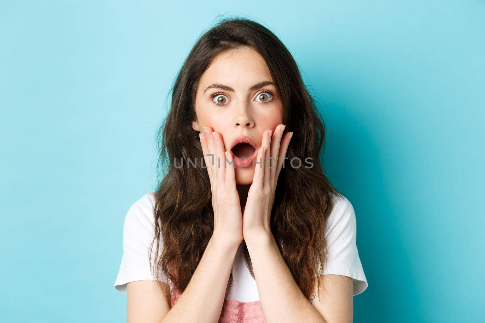 Oh my gosh. Close up portrait of shocked girl face, touching head and staring at camera startled, hear bad news, standing over blue background by Benzoix