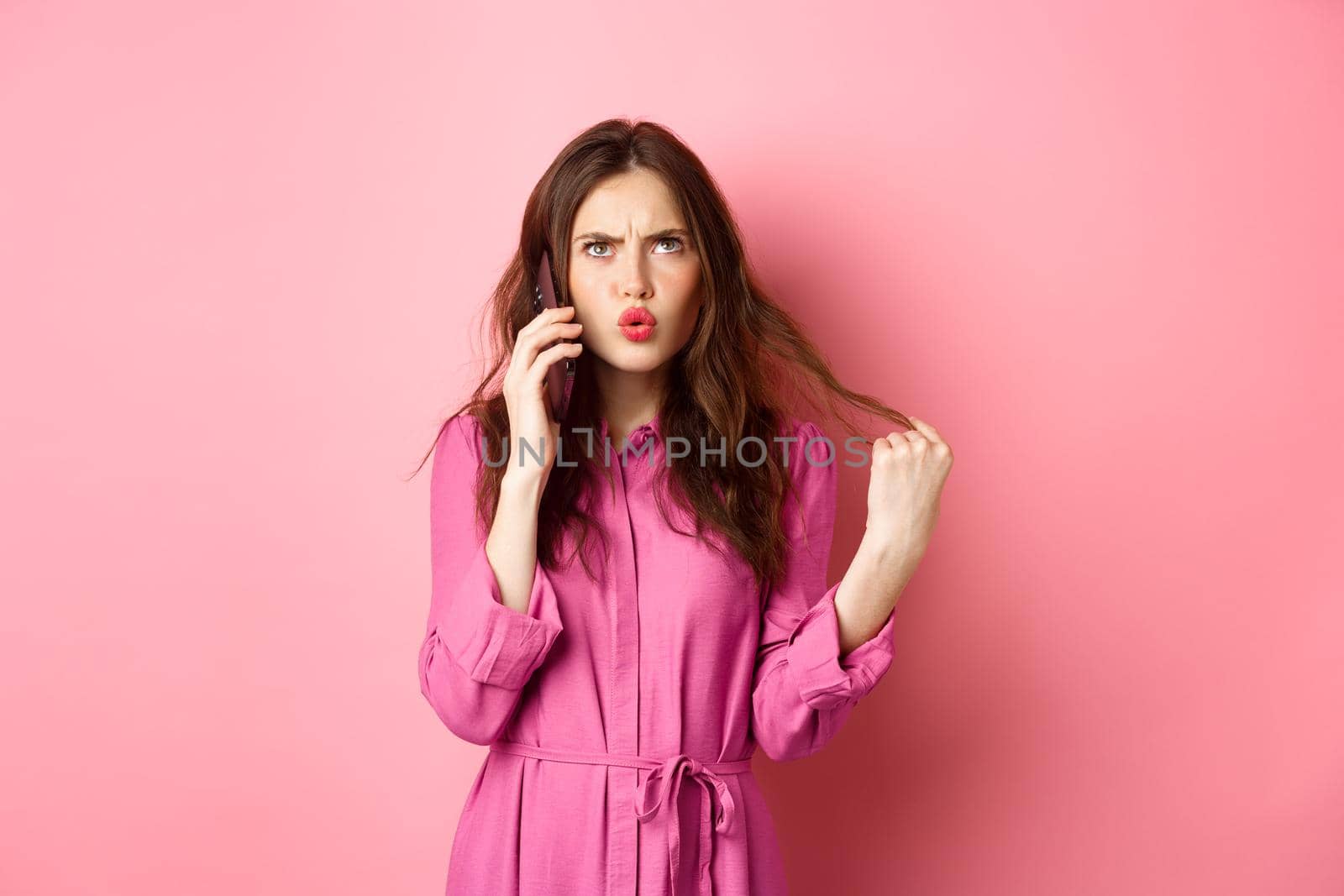 Young woman answer phone call, looking confused and indecisive, making takeaway order on smartphone, standing against pink background.