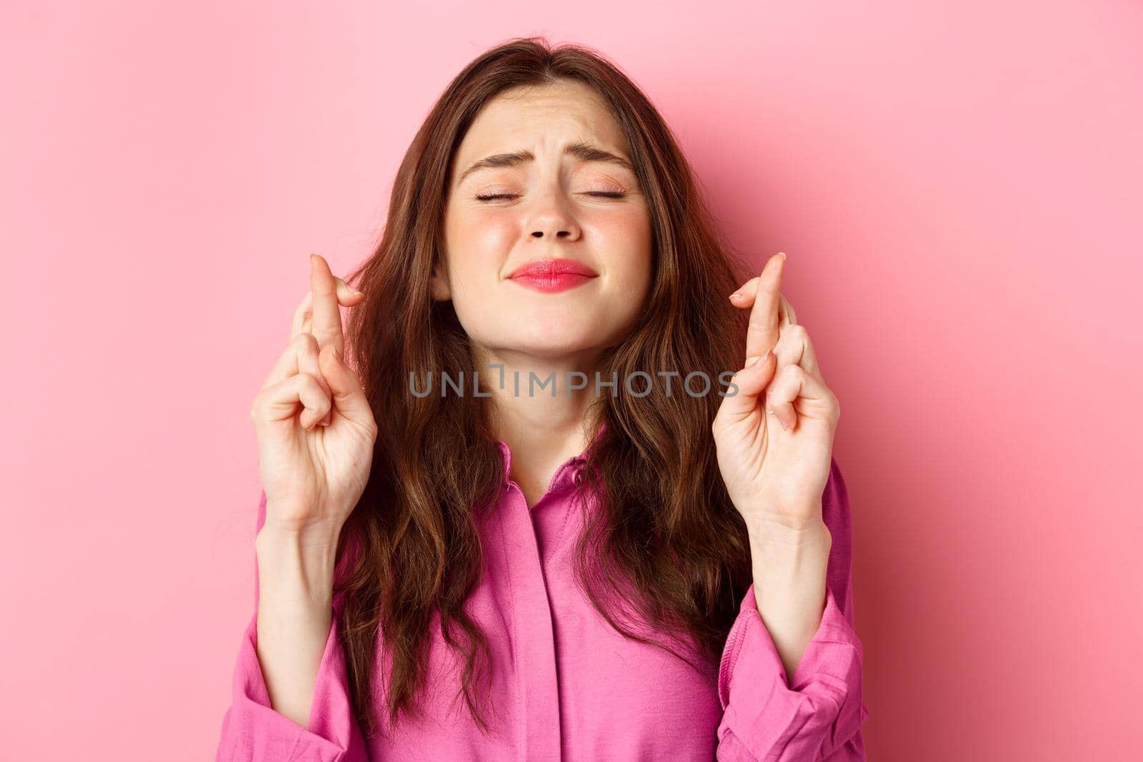 Close up of hopeful desperate woman begging god, holding hands in pleading gesture and close eyes, say please, standing over pink background.