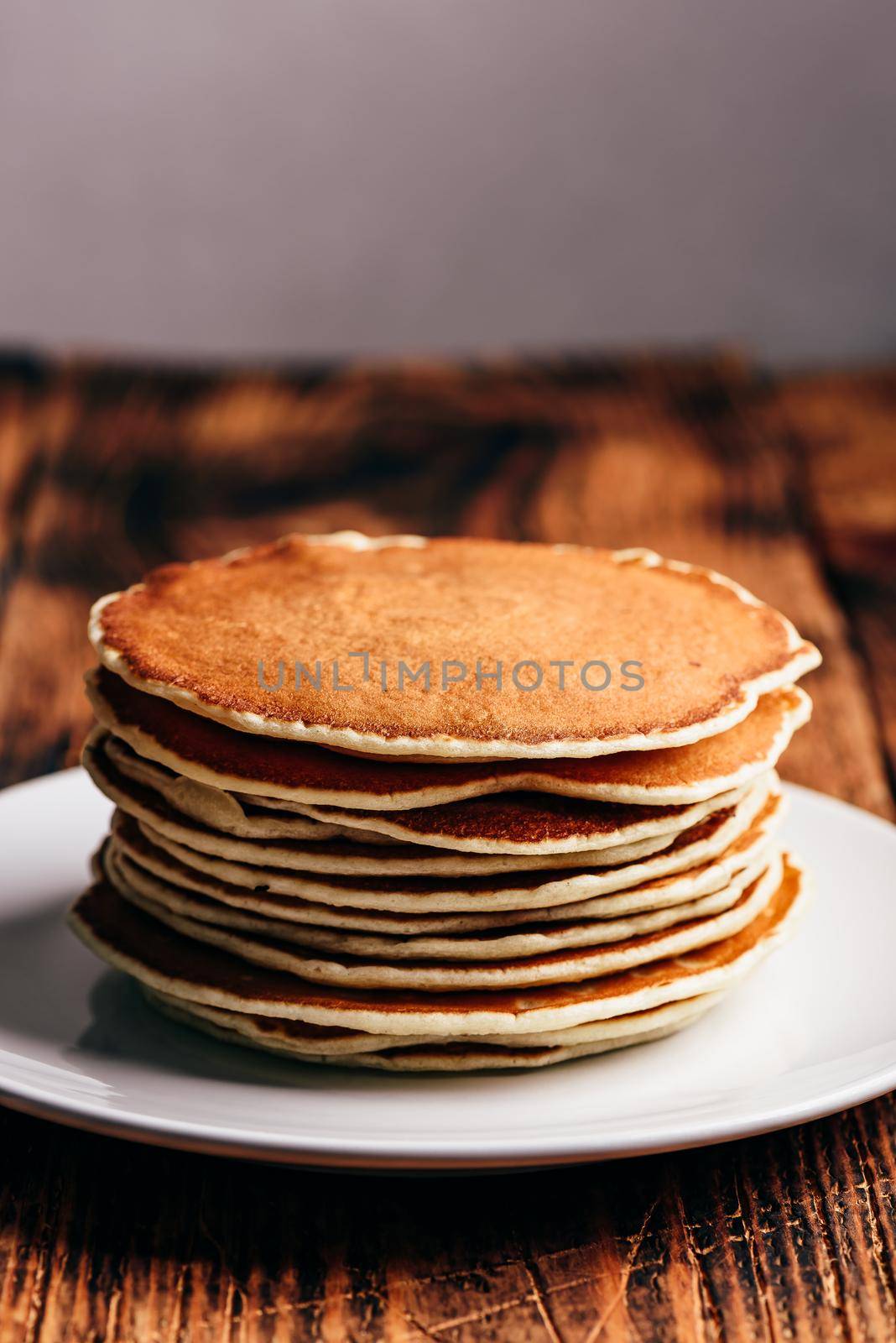 Stack of american pancakes on white plate over wooden table