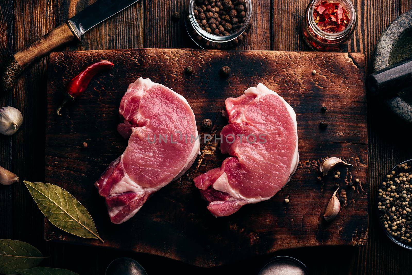 Two raw pork loin steaks on chopping board