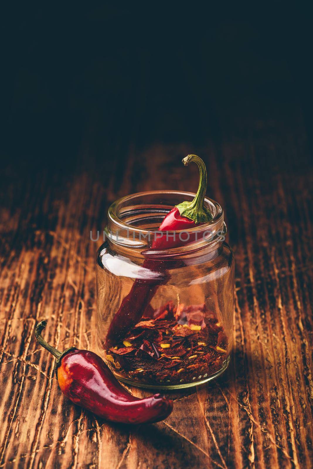 Two dried red chili peppers in jar with ground peppers