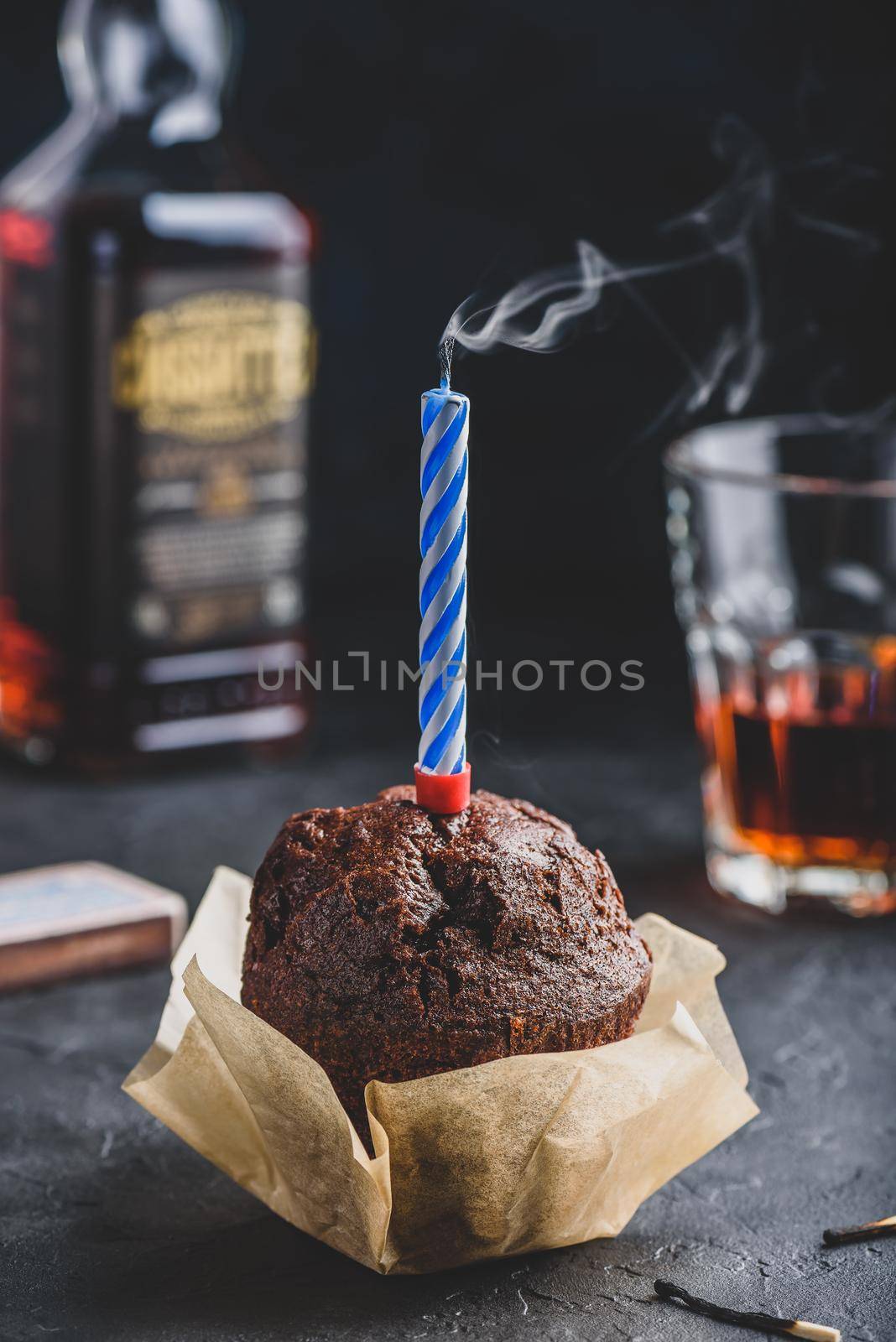 Birthday chocolate muffin with smoking candle on dark concrete background
