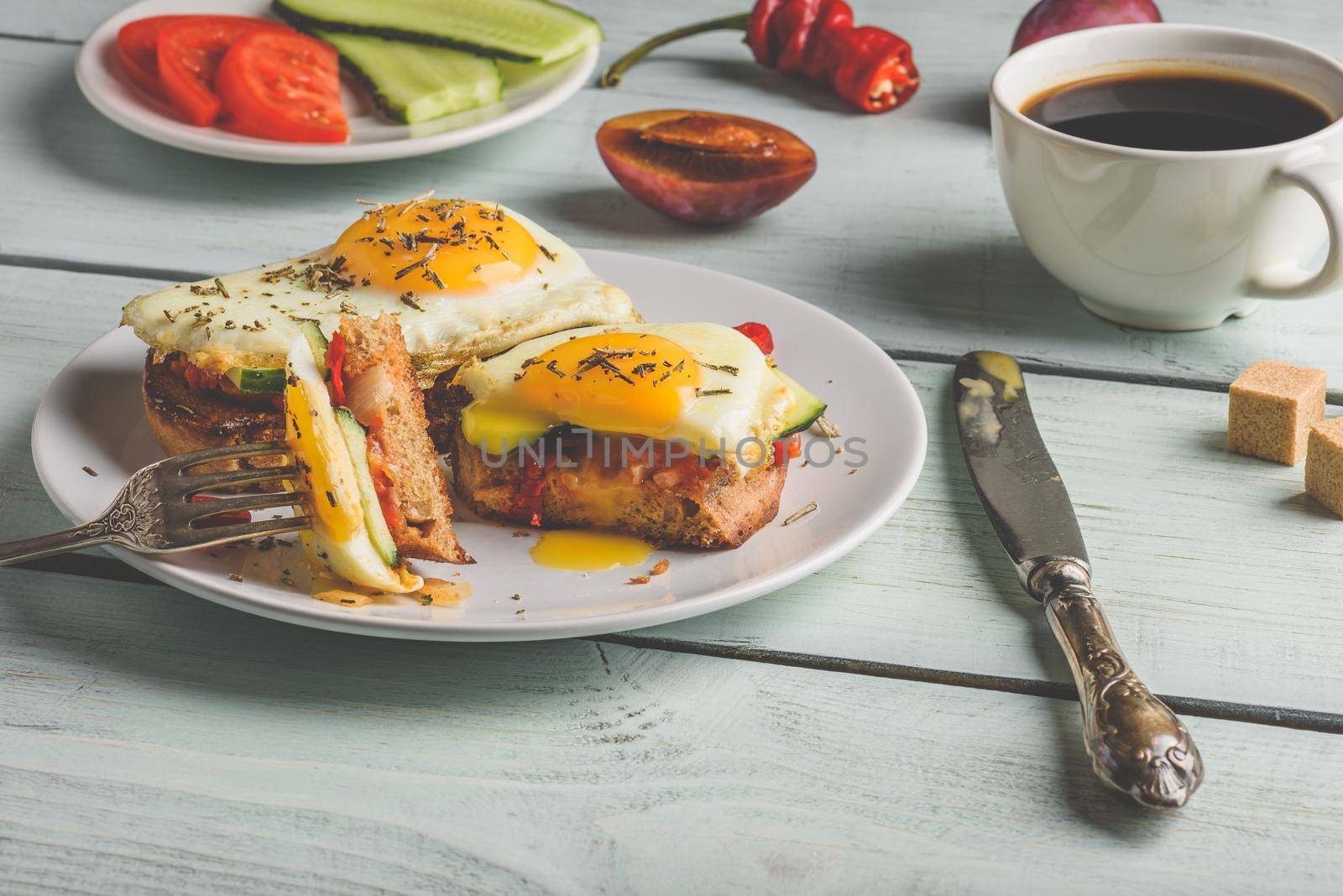 Breakfast toasts with vegetables and fried egg on white plate, cup of coffee and some fruits over wooden background. Clean eating food concept.