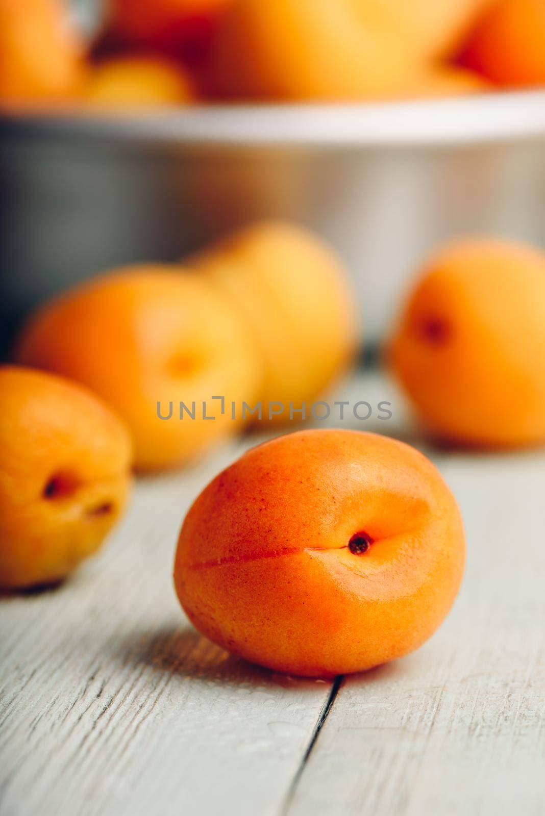 Mellow apricots over light wooden surface and metal bowl with fruits on background