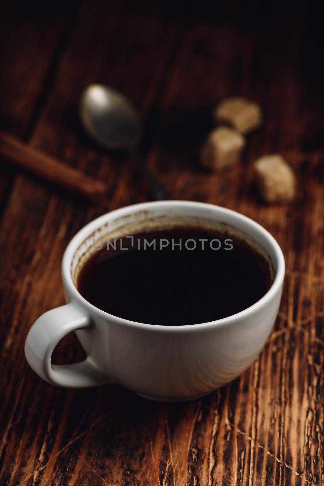 Black coffee in white cup with sugar and cinnamon sticks