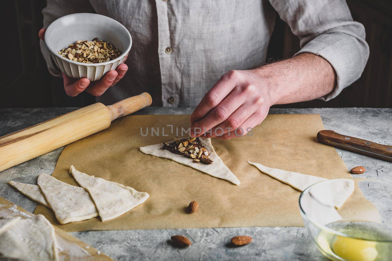 Homemade croissant preparing. Baker sprinkles chopped almonds on top of hazelnut spread