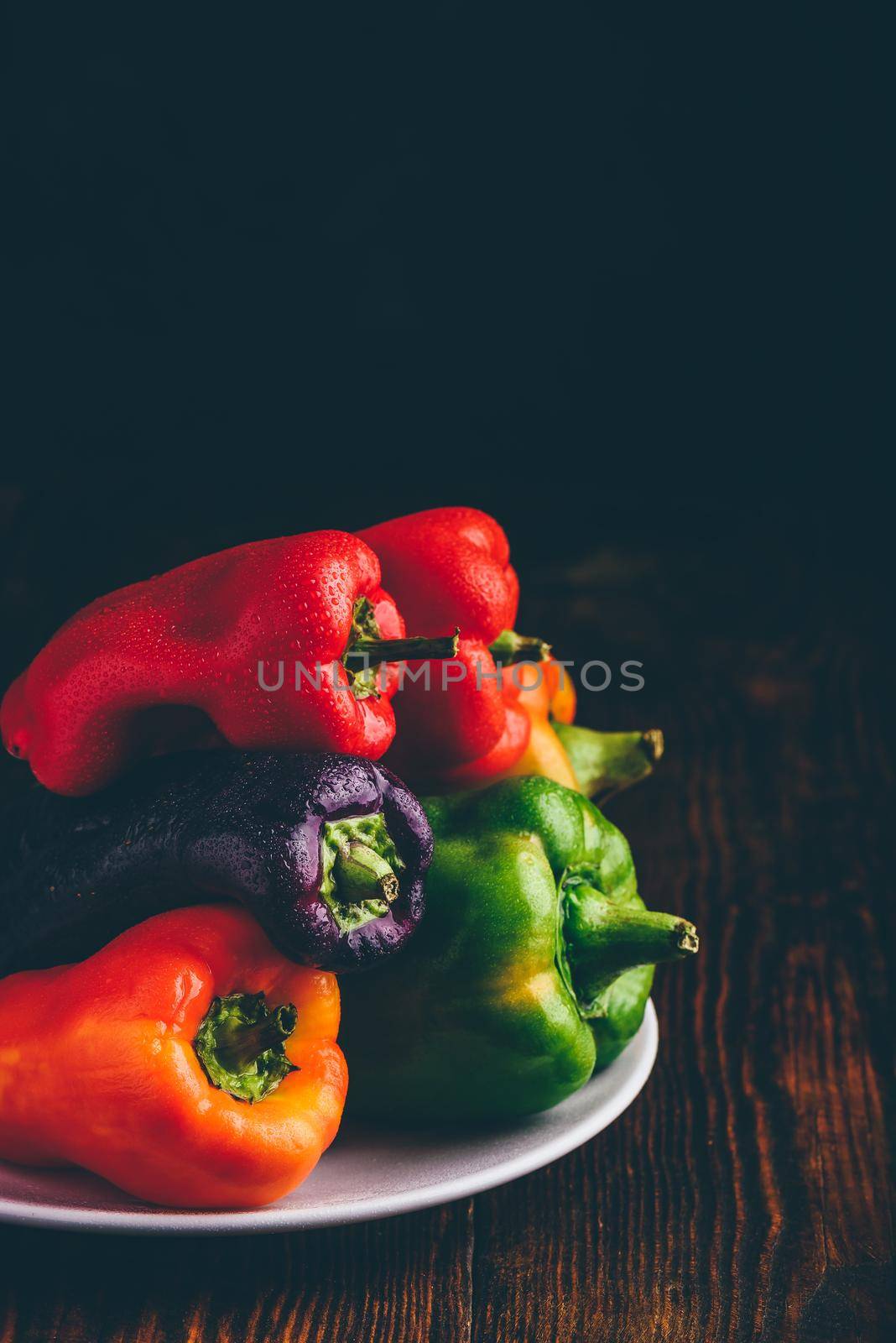 Multicolored fresh bell peppers on plate over wooden background