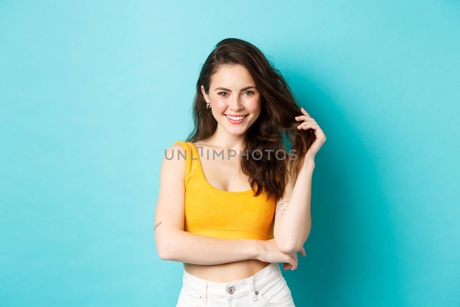 Summer and lifestyle concept. Young attractive woman playing with her hair, standing in cropped top for summertime vacation, look determined and cunning at camera, smiling pleased.