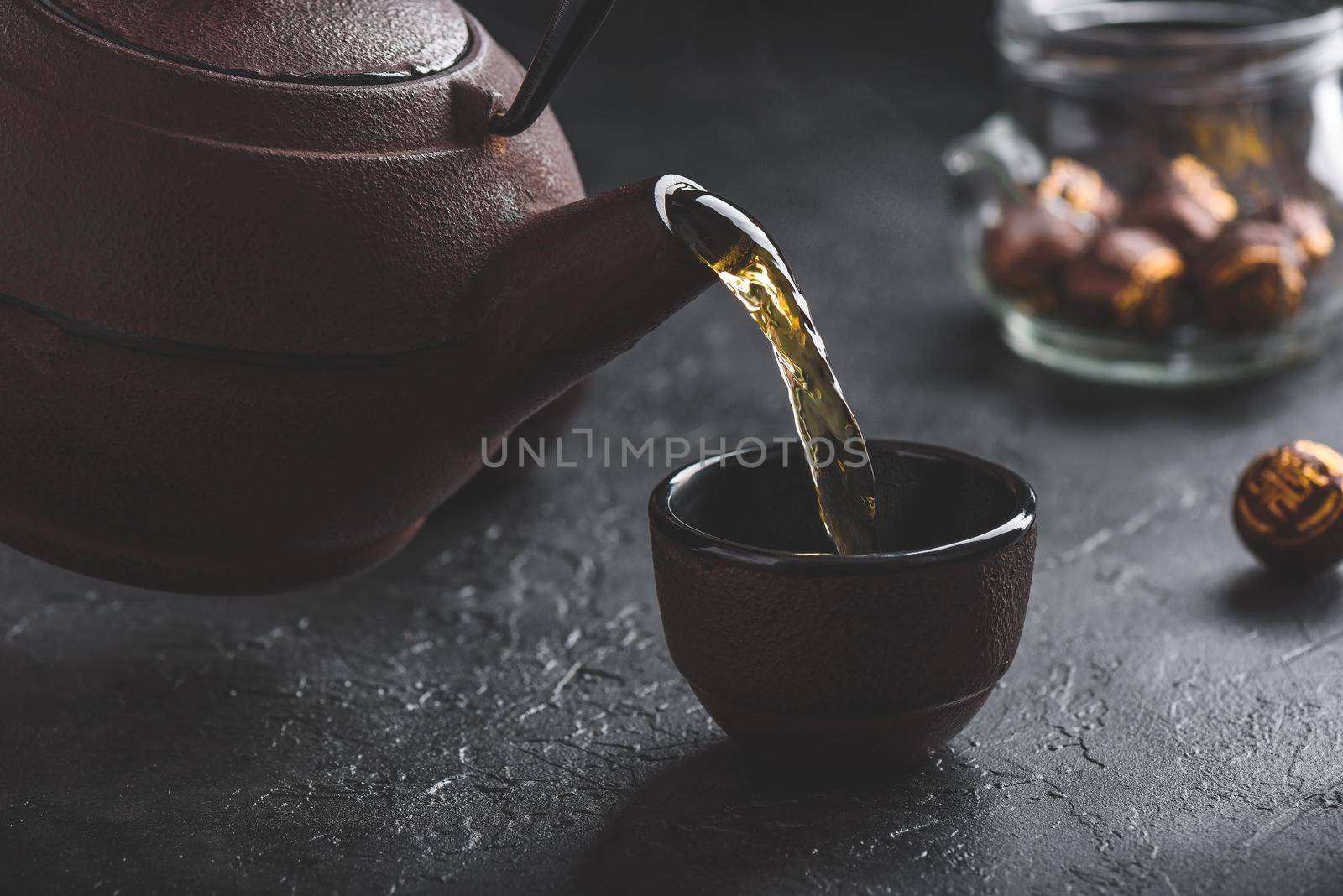 Pouring ready red tea from iron kettle into tea bowl