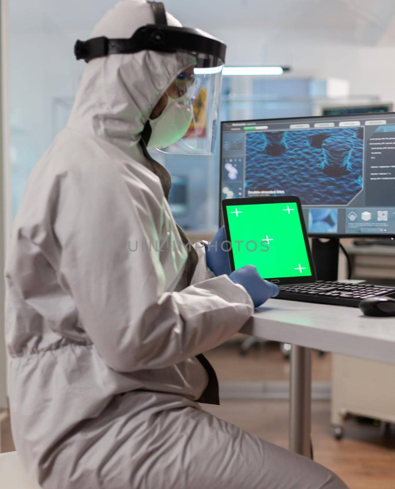 Chemist man wearing protection suit holding tablet with green mockup. Team of microbiologists doing vaccine research writing on device with chroma key, isolated display.