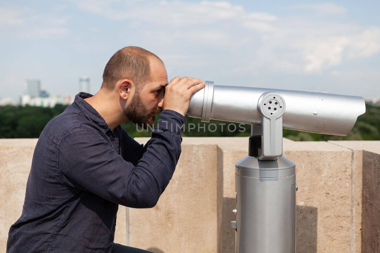 Man tourist standing on building rooftop looking through binocular telescope by DCStudio