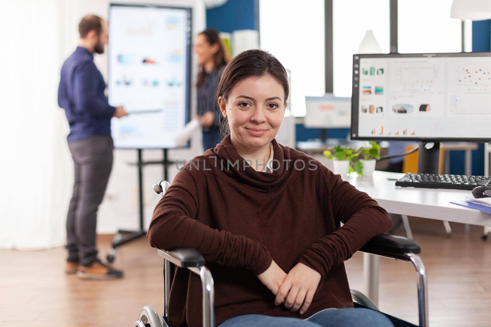 Close up of paralysed disabled invalid handicapped woman work colleague looking at camera smiling working in economic business office at computer with data, prosessing financial information.