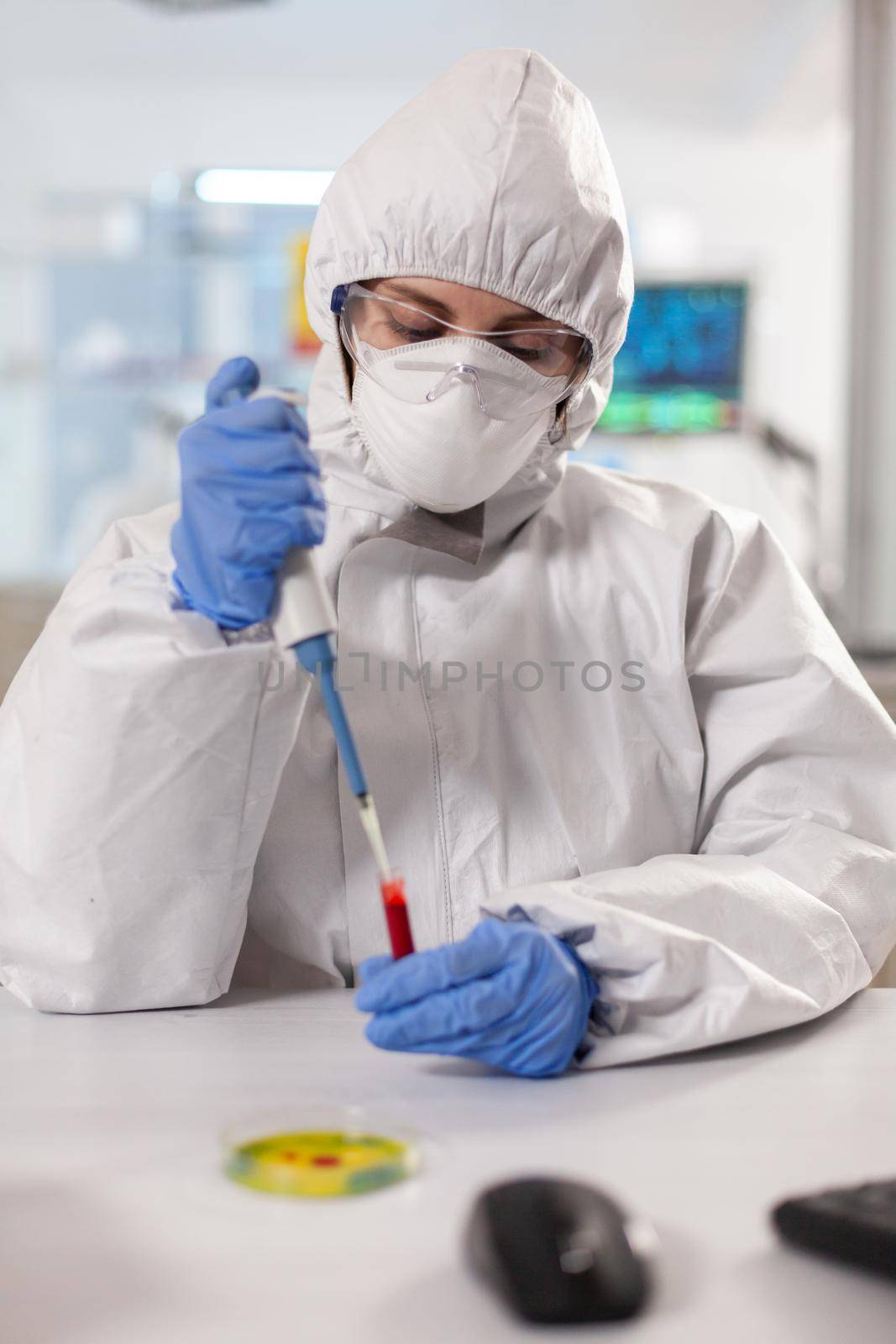 Scientist dressed in ppe suit taking blood sample using micropipette by DCStudio