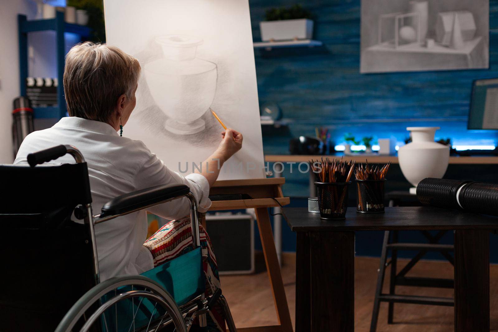 Old woman with disability creating drawing of vase from table by DCStudio
