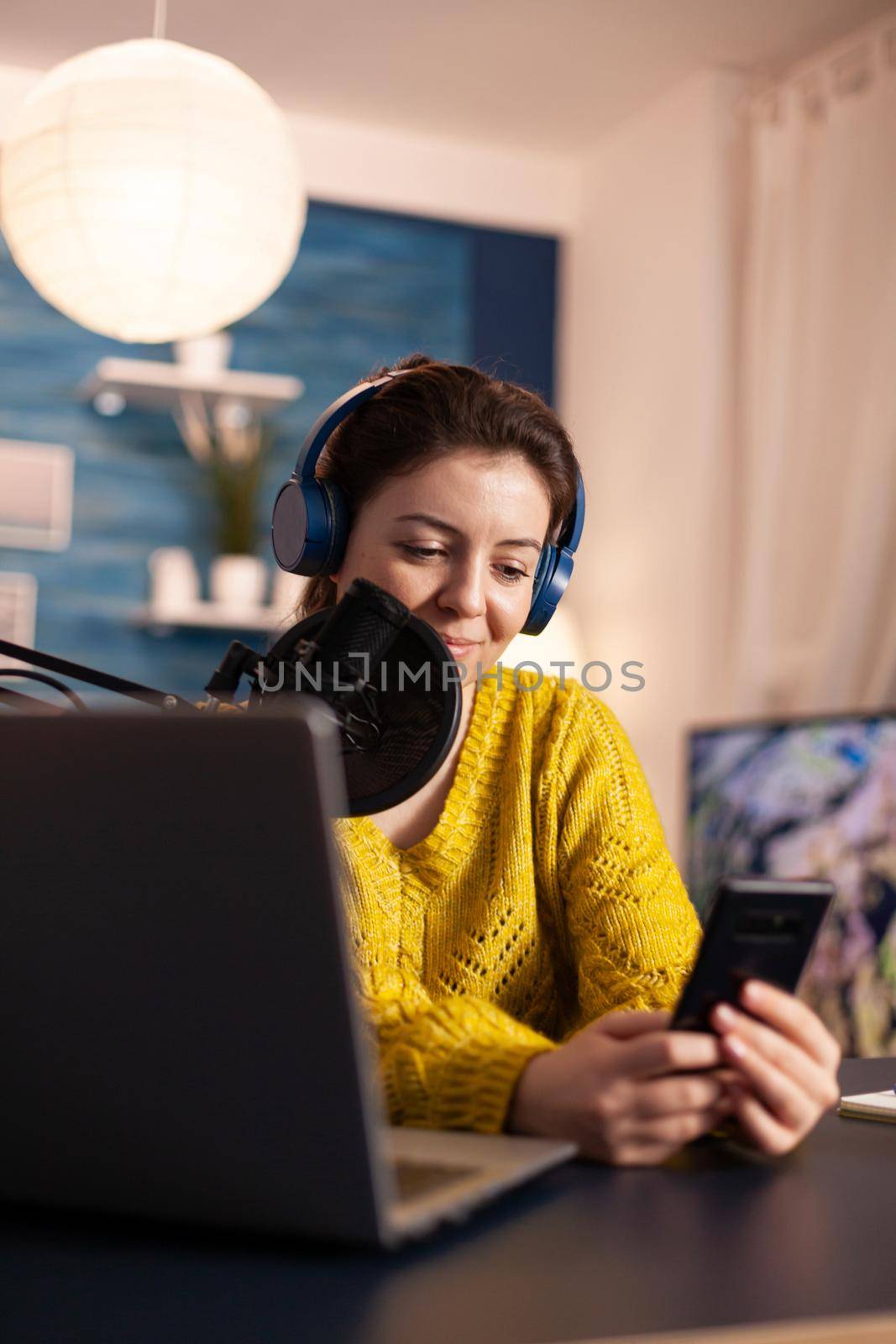 Blogger woman recording video for her blog in home studio reading messages on smartphone. On-air online production internet broadcast show host streaming live content for social media.