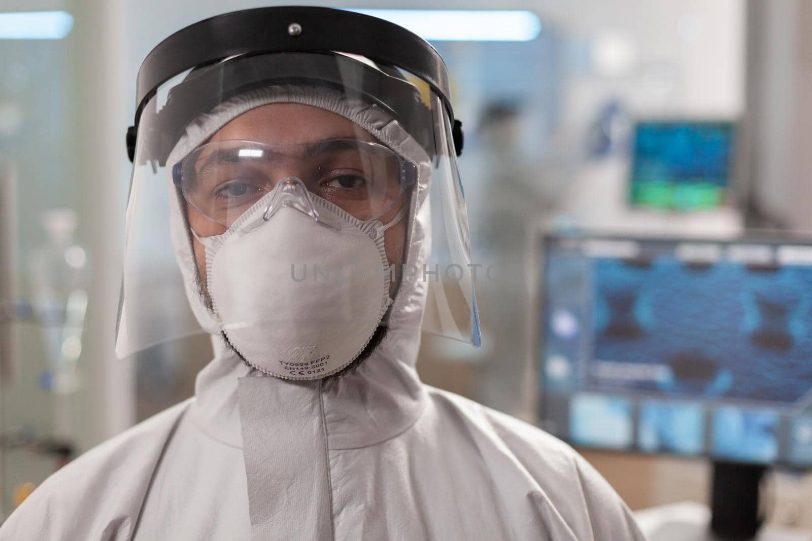 Tired laboratory doctor in protection suit and looking at camera. Team of scientits examining virus evolution using high tech and chemistry tools for scientific research, vaccine development.