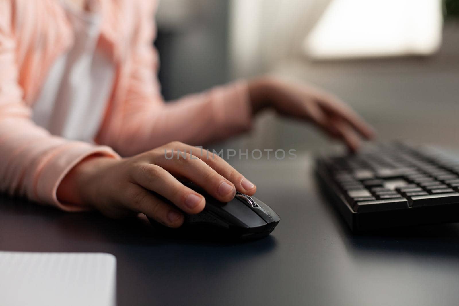 Close-up little schoolkid hands typing literature homework using computer keyboard sitting at desk studying online school lesson in living room. Concept of distance education at home