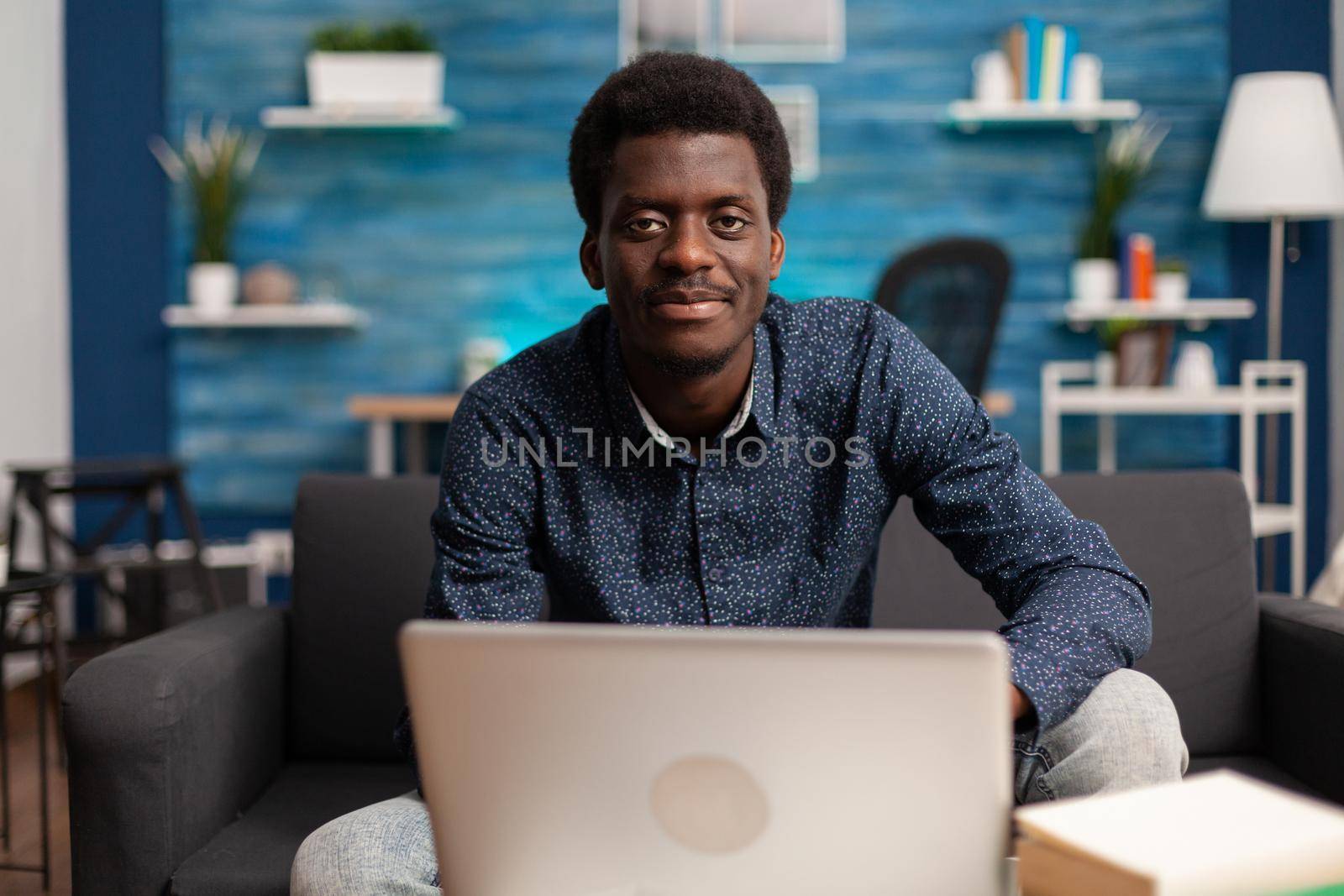 Portrait of african american student working at online management lesson browsing academic information on laptop in living room. Ethnic man using e-learning school platform. Computer user