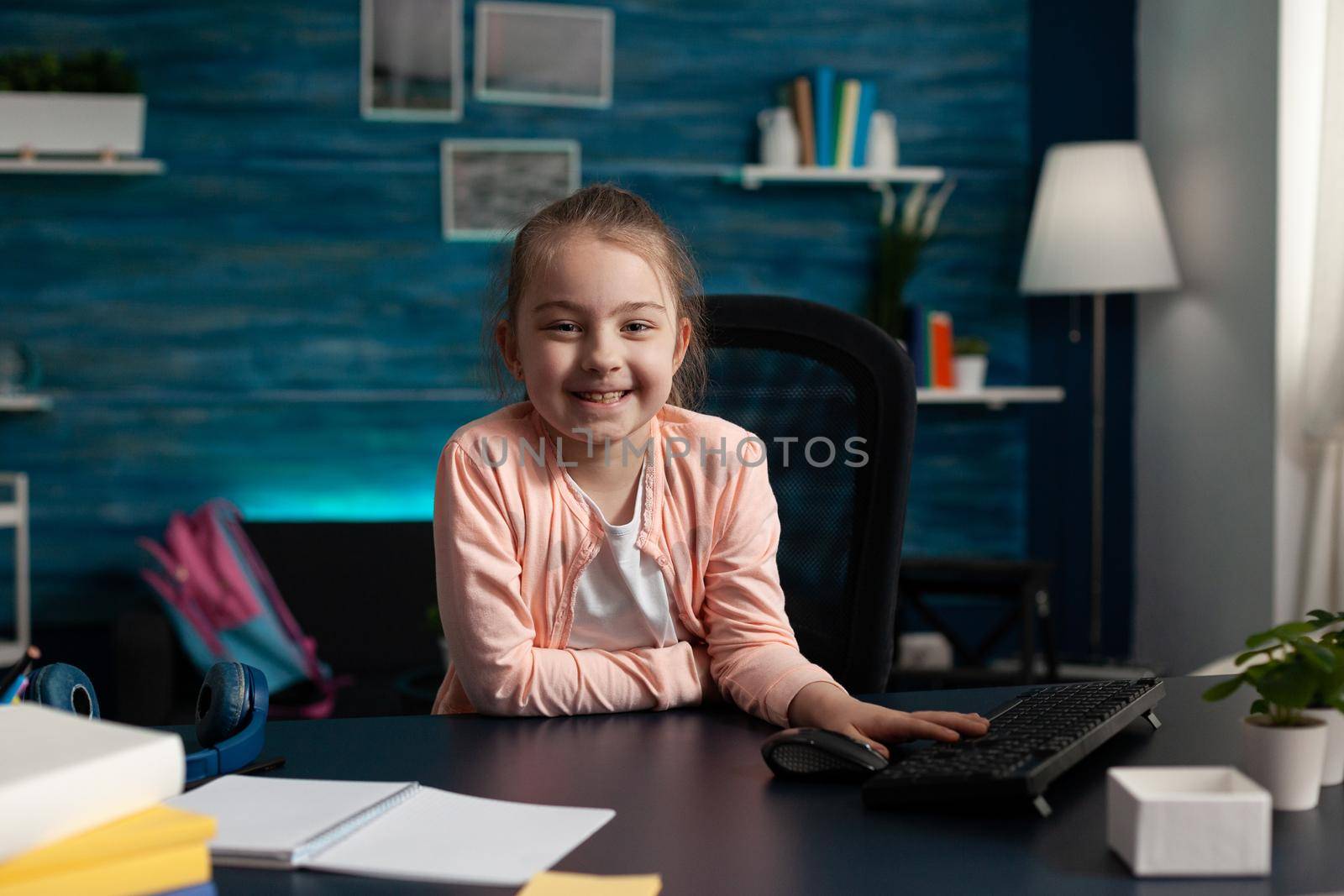 Portrait of smiling little schoolchild sitting at desk table in living room studying online literature lesson working at school homework during home schooling. Child using elearning classwork platform