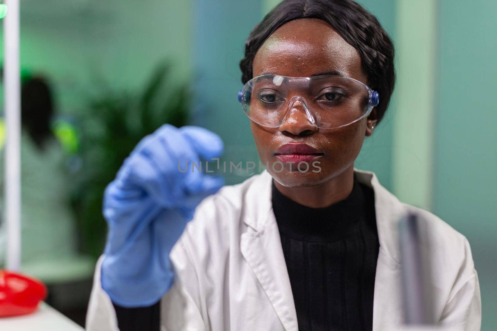 Botanist researcher scientist analyzing green liquid sample under microscope for microbiology experiment. Chemist specialist discovering organic gmo plants while working in pharmaceutical laboratory.