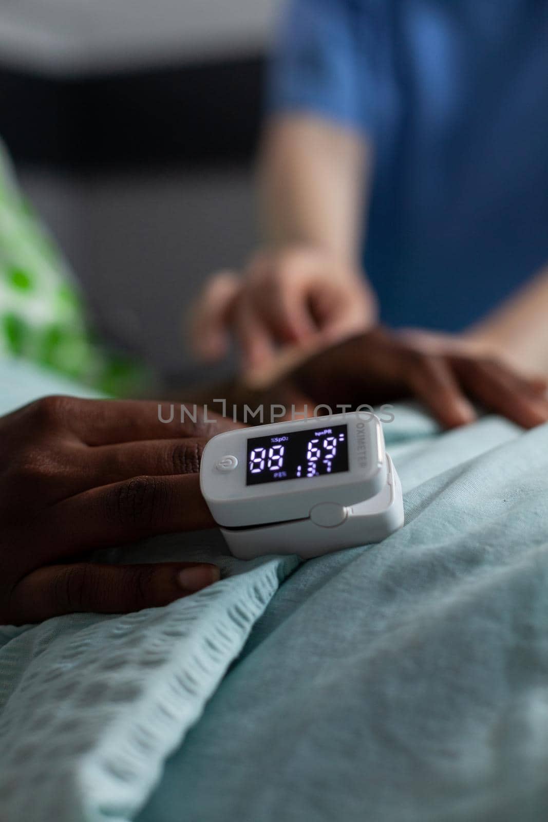 Close up of oximeter on african american girl hand laying in hospital ward bed. Device showing low oxygen saturation and pressure measurement used on young patient with disease. Medical equipment