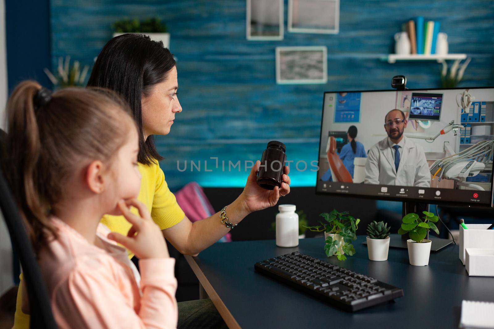 Parent discussing daughter sickness with remote physician holding pills bottle in hands during online videocall meeting conference. Virtual consultation telemedicine on computer screen